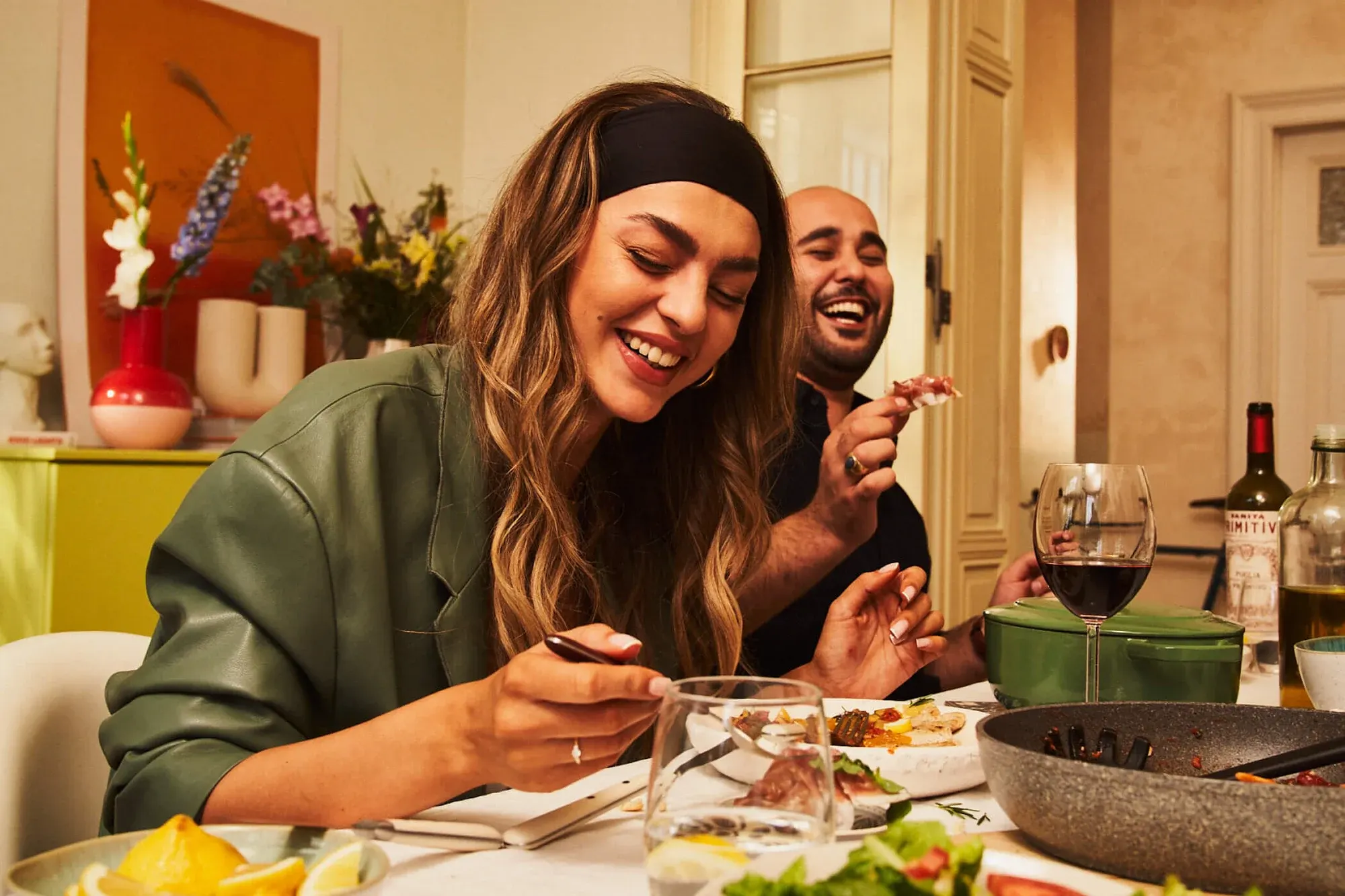 Two friends laughing over lunch at a table set with Ballarini cookware