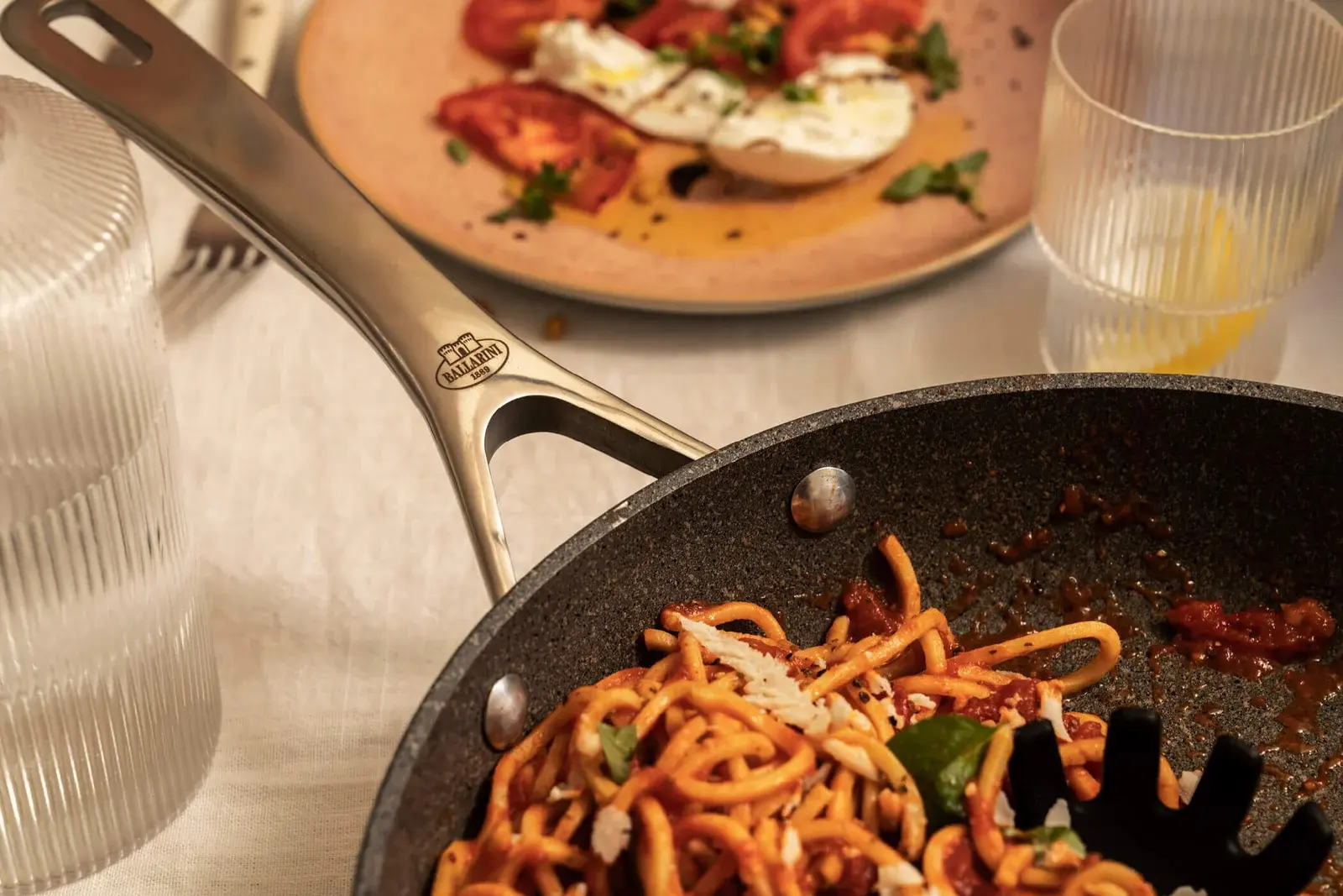 A Ballarini frying pan of spaghetti with tomato sauce on a set table